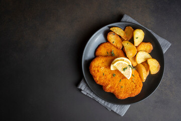Chicken schnitzel with sauce, fried potatoes and lemon in a plate