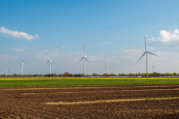 landscape shot of a field with five wind turbines behind it