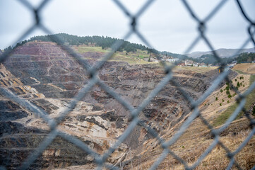 Open pit mine in background with a blurred chain link fence in the foreground. 