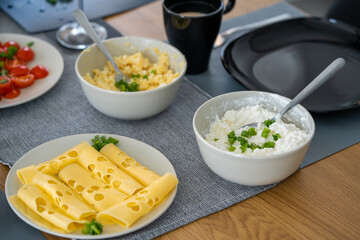 homemade breakfast, yellow cheese with holes, small sliced tomatoes, cottage cheese, egg paste, eggs, chives, tea, orange, carrot and grapefruit juice in wine glasses, black tableware.