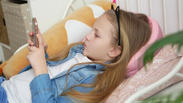 a pretty little girl in a rim with cat ears with a phone in bed. 
