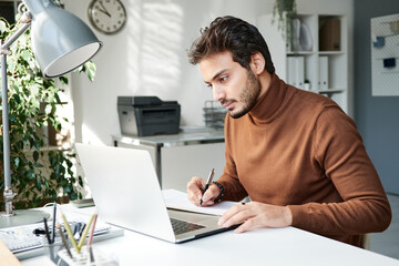 Thoughtful young middle eastern manager in brown sweater using laptop while preparing project plan