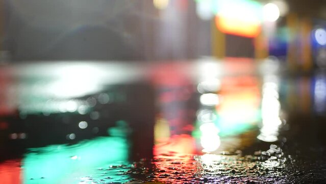 Neon lights reflection on road in rainy weather. Rain drops on wet asphalt of city street in USA. Puddle of water on pavement or sidewalk. Rainfall at night. Abstract seamless looped cinemagraph.