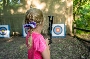 Young girl at summer camp learning to use a bow and arrow looking down field at the target.