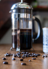 Photograph of coffee beans on a table next to a French press full of coffee.
