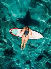 Surf girl with surfboard in transparent ocean. Aerial view with surfer woman