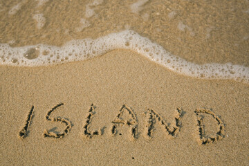 Island - handwritten on the soft beach sand.