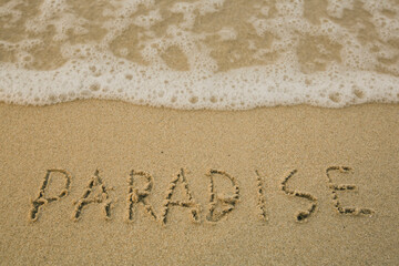 Fototapeta na wymiar Paradise - handwritten on the soft beach sand.