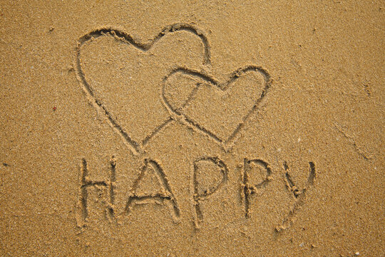 Two hearts and the inscription Happy is drawn on the beach sand.