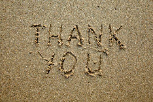 Thank you â€“ handwritten inscription on the soft beach sand.