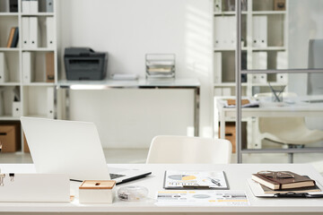 Fototapeta na wymiar Office interior with white table with open laptop, financial documents and organizer and chair