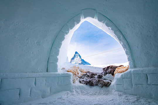 Famous matterhorn peak against sky seen through igloo. Snow covered fur at entrance of ice house. Interior of frozen hut in alpine region during winter.
