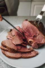 hand slicing Kurobuta bone-in ham meat on kitchen counter with knife and fork	
