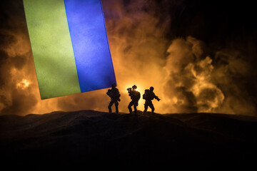 Russian war in Ukraine concept. Silhouette of armed soldiers against Ukrainian flag and burned out...