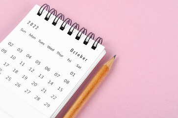 October 2022 desk calendar with wooden pencil on pink background.