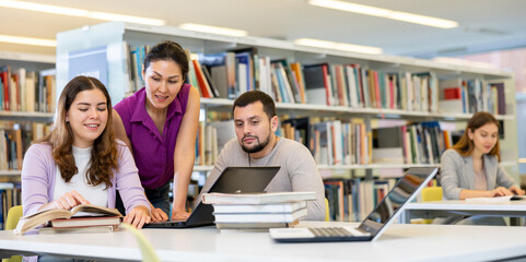 Group of people looking at laptop screen together in library and preparing for exam