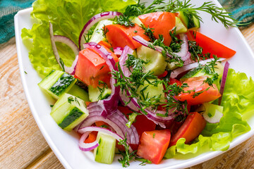 Vegetable salad with tomatoes and cucumbers and red onion on wooden table macro close up