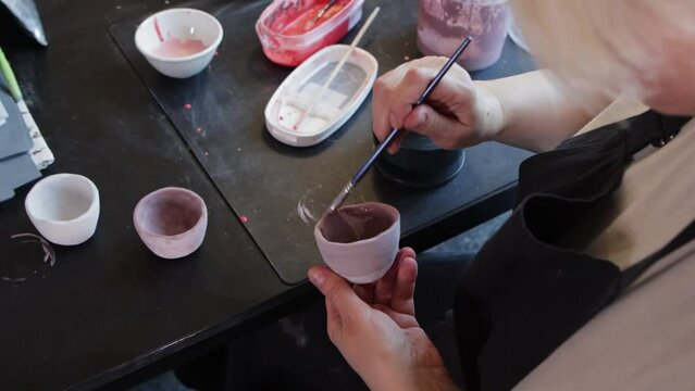 An elderly woman painting ceramic mug in dusty purple