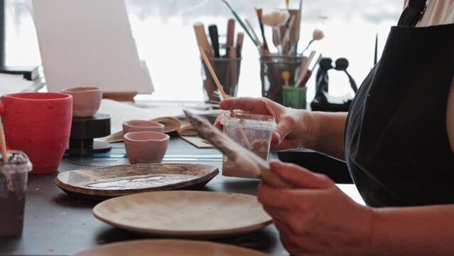An elderly woman pours beige and brown paints on the plate