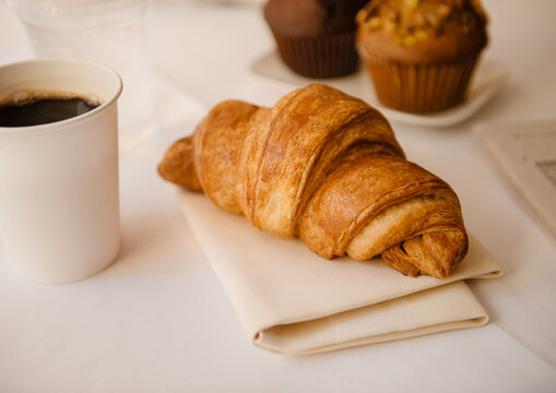 croissant with coffee and breakfast muffins in the background