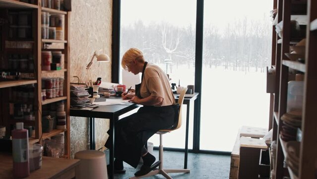 An elderly woman artist working by the table in the workshop - drawing a sketch