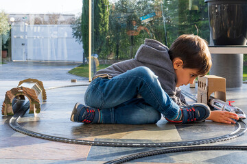 Young kid playing with toy trains on the floor. Toy train similar to Cercanias Renfe Spanish train and Ave high speed train
