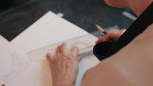 An elderly woman sketching design for a new clay item using pencil and ruler