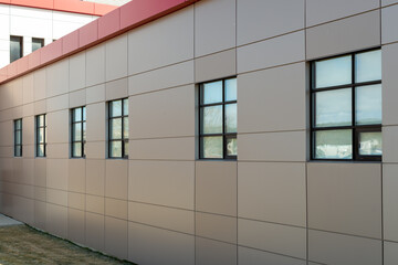 The exterior wall of a contemporary commercial style building with aluminum metal composite panels and glass windows. The futuristic building has engineered diagonal cladding steel frame panels.