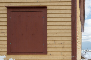 The exterior corner of an old wooden building. The wood lat clapboard walls are yellow in color...
