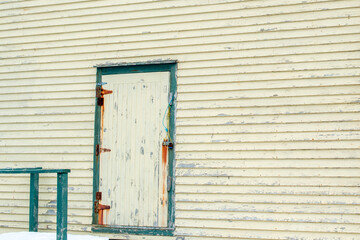The exterior of a large wooden building with pale yellow clapboard siding. There's a small wood...