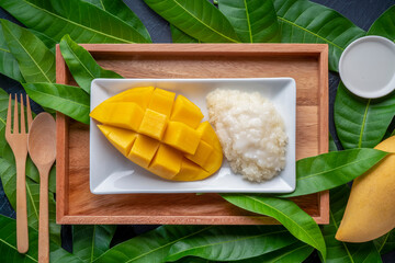 Sticky rice with mango and coconut milk on white plate over mango leaf, Sweet Mango Sticky Rice with Coconut Milk.