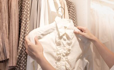 Female hand choosing clothes for checked pattern cotton polo shirt on the rack in cloth shop at a department store.