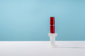 Red lipstick on roman marble column on blue background. Creative product stage mock up, cosmetic...
