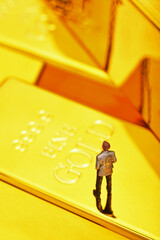 Miniature people figure businessman stand on pile of gold bar. 