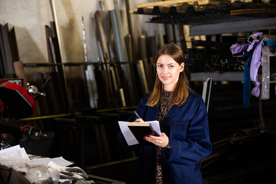 Mechanical metalworking factory workwoman noting measurement or order data in notebook..