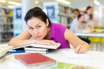 Tired woman resting her head on stack of books in public library