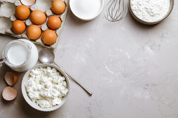 Cottage cheese in a ceramic bowl, jug of milk, flour and eggs. Ingredients for cooking. Top view 