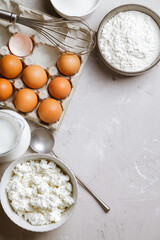 Cottage cheese in a ceramic bowl, jug of milk, flour and eggs. Ingredients for cooking. Top view 