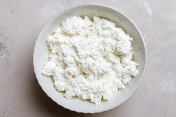 Cottage cheese in a ceramic bowl on a gray background. Top view 
