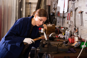 Fototapeta na wymiar Young woman mechanic working with hand hammer in workshop