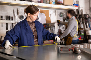 Focused young workwoman measuring metal parts in metalworking workshop