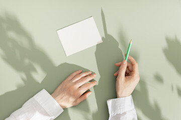 Woman hold pencil, blank paper card on olive green color background, copy space. Minimalist summer...