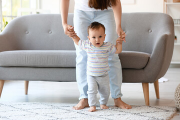 Little baby boy learning to walk with his mother's help at home