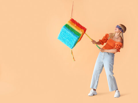 Young Woman With Blindfold Breaking Mexican Pinata On Beige Background