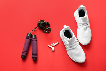 Skipping rope, earphones and shoes on red background