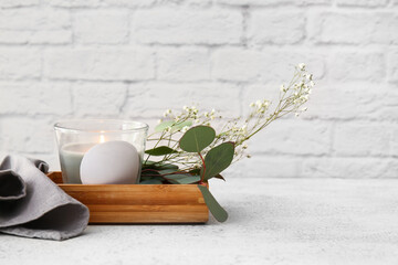 Wooden box with burning candle and flowers on light table, closeup