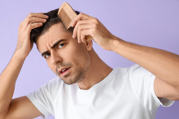 Worried young man combing hair on lilac background, closeup