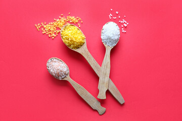 Wooden spoons with different sea salt on red background