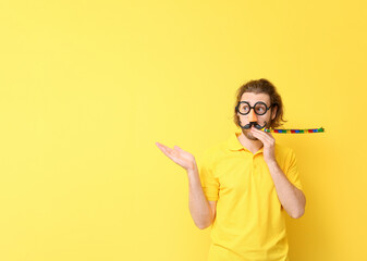 Funny young man in disguise and with party whistle showing something on yellow background. April...