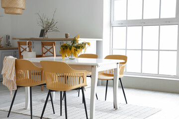 Stylish interior of light kitchen with mimosa flowers on dining table
